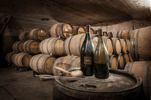 two bottles of wine in a winery, in front of many wine barrels